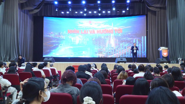 Khán phòng lớn có nhiều người ngồi trên hàng ghế màu đỏ hướng mắt lên sân khấu, nơi một diễn giả đang phát biểu trước màn hình LED lớn hiển thị dòng chữ "Nhìn lại và hướng tới" - Ảnh 4.