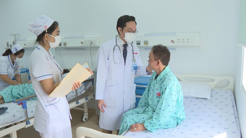 Bác sĩ đeo khẩu trang và ống nghe đang động viên người bệnh cao tuổi ngồi trên giường bệnh cùng điều dưỡng - Ảnh 4.