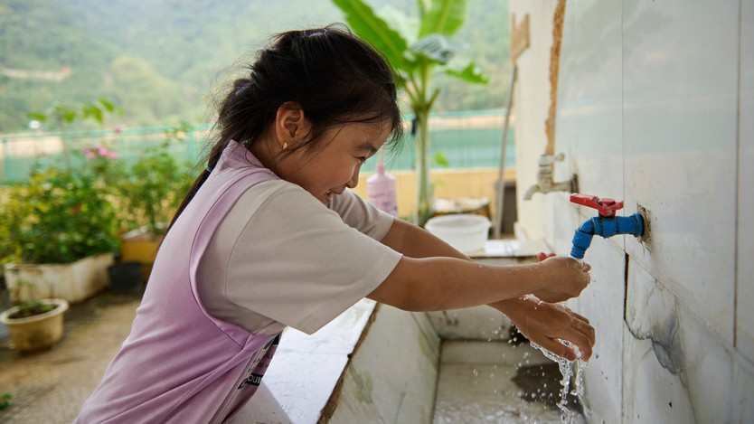 Một học sinh rửa tay ngoài trời trong bồn rửa lớn có vòi nước tại Trường Tiểu Học và Trung Học Cơ Sở Hiền Lương. 